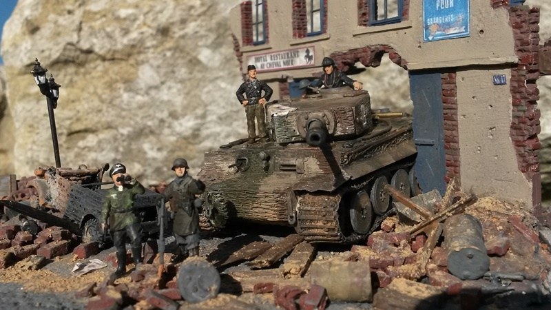Ein schwerer Kampfpanzer Pz.Kpfw. VI Tiger durchbricht ein Holztor, da die Straßen durch zahlreiche Trümmerteile fast unpassierbar sind.